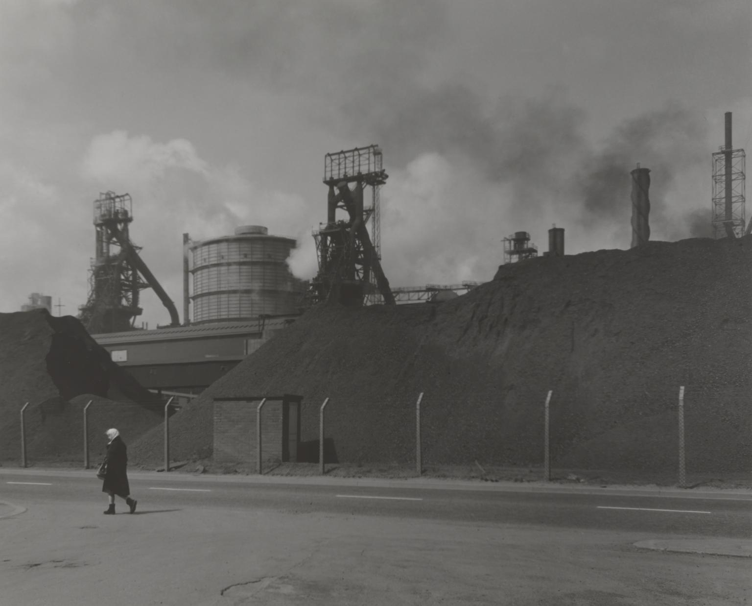 P81023: Woman walking past blast furnaces, Grangetown, Teeside