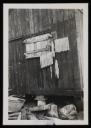 Prunella Clough, ‘Black and white photograph of the side of a wooden hut with lengths of string or twine hung out to dry’ [1950s]