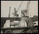 Prunella Clough, ‘Black and white photograph of a flat bed lorry loaded with boxes and parcels with cranes in the background’ [1950s]