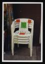 Prunella Clough, ‘Colour photograph of white plastic garden chairs stacked up outside a shop’ [1990s]