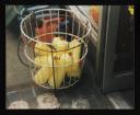 Prunella Clough, ‘Colour photograph of yellow bottles of washing-up liquid in a wire basket outside a shop’ [1990s]