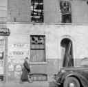 Nigel Henderson, ‘Photograph of an unidentified woman walking past a derelict building’ [c.1949–c.1956]