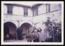 Unknown Photographer, ‘Photograph of a group of three unidentified people, two women and a man, standing in a courtyard with citrus fruit trees and bright red geraniums in the background’ August 1965 