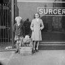 Nigel Henderson, ‘Photograph of two unidentified girls outside a doctors surgery with a stuffed figure in a box’ [1949–54]