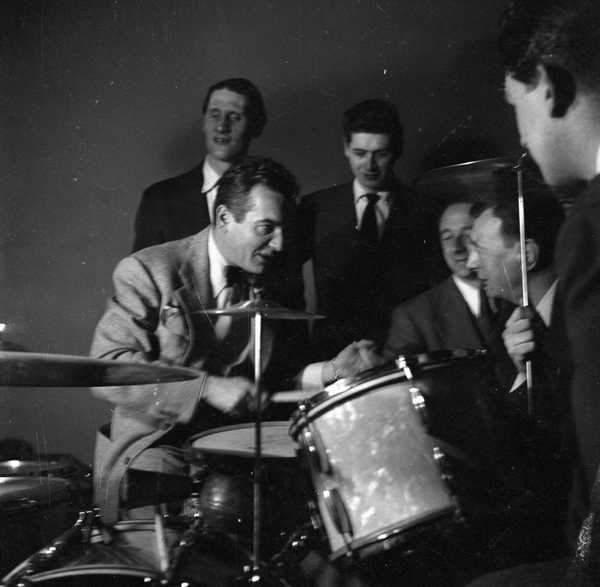 Photograph of five men surrounding a man performing on drums‘, Nigel ...