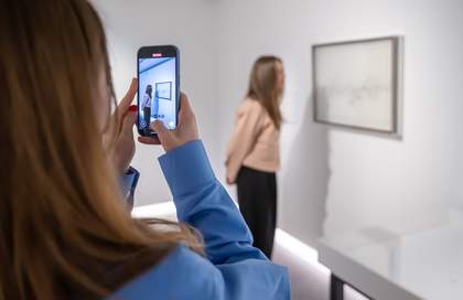 A photograph of a woman taking a photo of another woman standing next to an artwork.