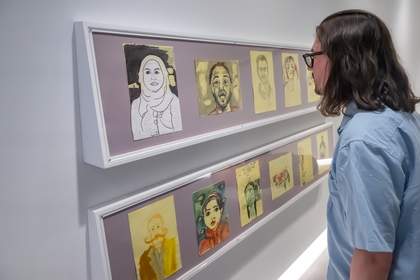 A photograph of a man in a light blue shirt looking at an artwork which features drawings on yellow paper.