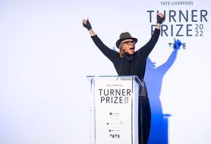 Woman with arms in the air behind a podium and in front of white screen.
