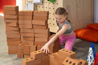 A young girl is sitting on the floor playing with brick blocks.