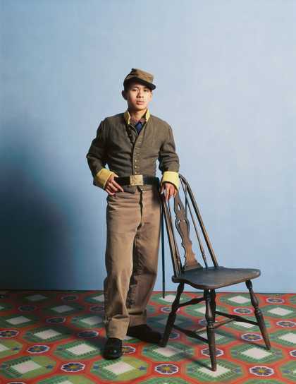 A man in an army uniform stands in front of a chair