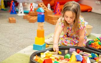 A young girl is sitting on the floor playing with colourful building blocks.