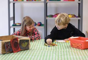 A photograph of two children sat at a craft table doing art activities.