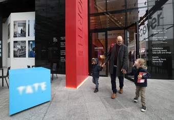 A photograph of a father holding the hands of his two sons whilst leaving Tate Liverpool + RIBA North