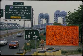 Keith Haring standing next to his Crack is Wack billboard