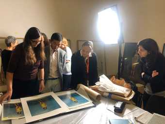 A group of people look at photographic prints on a tabletop with a bright studio light behind