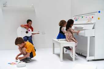 Children playing musical instruments covered with colourful dot shaped stickers in a white room.