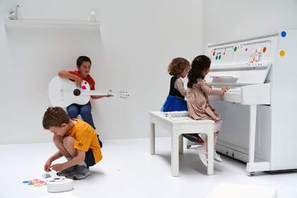 Children playing musical instruments covered with colourful dot shaped stickers in a white room.
