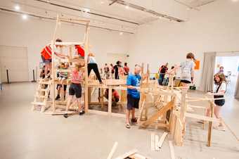 people construct a play area out of wood in a gallery space