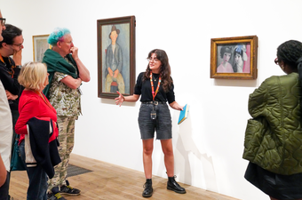 A member of Tate staff member talks to a group of visitors in front of a painting.