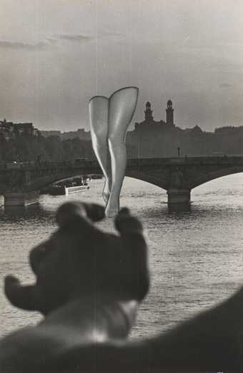 Collage using black and white photograph of a large hand holding a pair of human legs overlaid onto a photograph of the River Seine