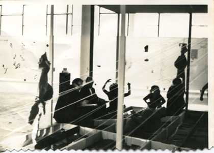 At the centre of the space, a circular raised stage containing figures trapped within a transparent plastic tent