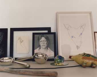 Photograph of a mantelpiece with miscellaneous objects including a few framed pictures and a toy fish.