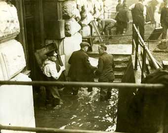 Photo of men rescuing pictures from a flooded Tate Britain. The men are bringing the pictures up an exterior set of steps up to ground level.