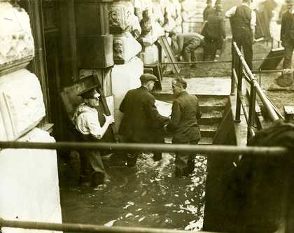 Photo of men rescuing pictures from a flooded Tate Britain. The men are bringing the pictures up an exterior set of steps up to ground level.