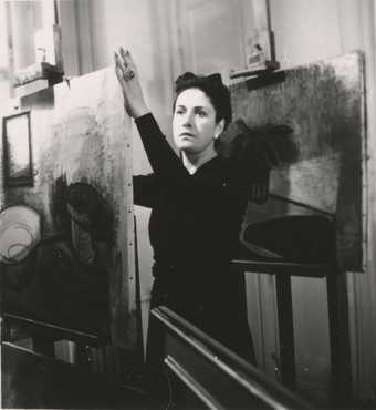 Black and white photograph of the artist Dora Maar standing by an easel