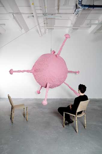 Back of figure sitting on one of two chairs looking at a round pink sculpture