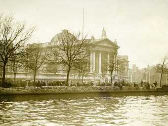 Photo of a Tate Britain and the river Thames with layers of sandbags along the river bank.