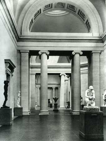 Black and white photo of the Duveen Gallery at the Tate Britain.  There are a few sculptures and a neo-classical style room.
