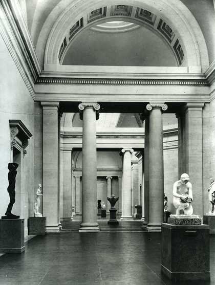 Black and white photo of the Duveen Gallery at the Tate Britain. There are a few sculptures and a neo-classical style room.