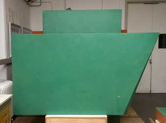 Patchy, whitish degraded coating and paint losses on the green box element of the sculpture.