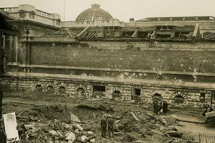 Sepia photo of the exterior of Tate Britain, a few people are looking at the bomb damage.