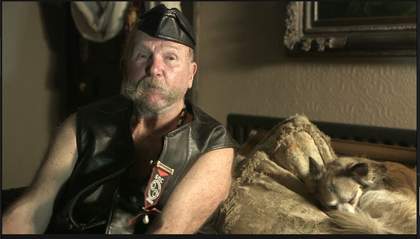 Older man dressed in leather sat next to a sleeping dog