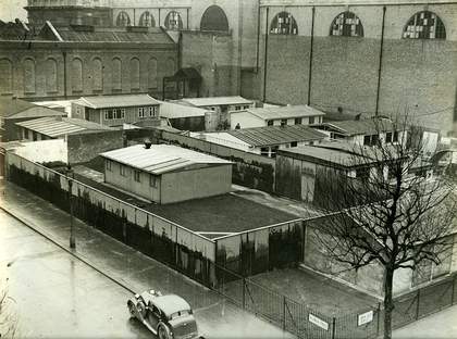 Black and white photo of temporary buildings in Tate Britain grounds. There is a car in the foreground.