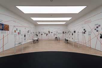 Gallery space with tables and chairs, and images on the walls connected by many dotted lines