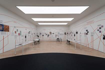 Gallery space with tables and chairs, and images on the walls connected by many dotted lines