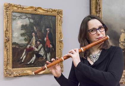 Hannah French poses with a replica of a baroque flute in front of Thomas Gainsborough’s Peter Darnell Muilman, Charles Crokatt and William Keable in a Landscape c.1750