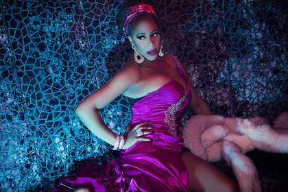 Portrait of Mzz Kimberley in a bright pink satin dress, holding a light pink fur coat