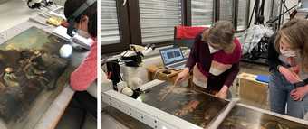 People working closely with a painting, which is lain horizontally on a workbench - one wears a head torch, there is surrounding technical equipment