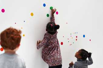 Children playing with colourful dot shaped stickers in a white room.