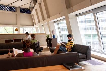 people sit on sofas and on a chair with a desk, reading books