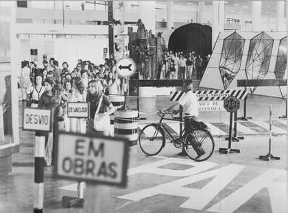 A pedestrian (zebra) crossing and street signs inside the biennial pavilion, a person wheeling a bicycle, and a crowd of visitors