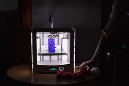 Someone operates a 3d printer in a dark room, it is printing a dark blue sculpture