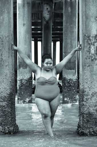 A person in a bathing suite stands with their hands up amongst some pillars in the sea