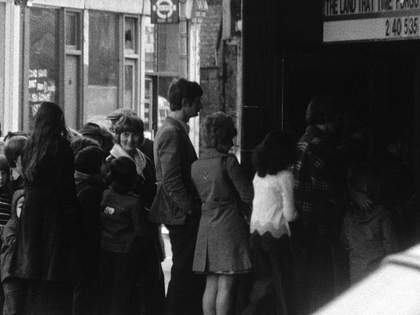 John Smith The Girl Chewing Gum 1976 (film still) close up of cinema queue
