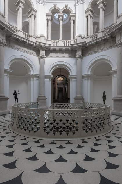 Front view of Tate Britain rotunda, the gallery is made of white stone with alcoves and pillars. There are statues in the alcoves and a balustrade.