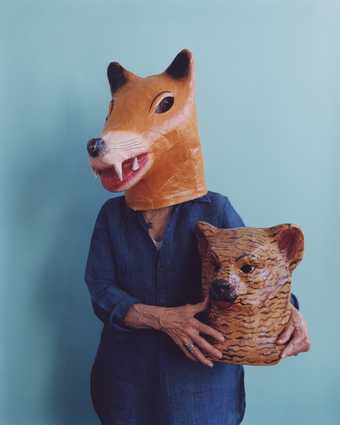Joan Jonas wearing a fox mask and holding a bear mask